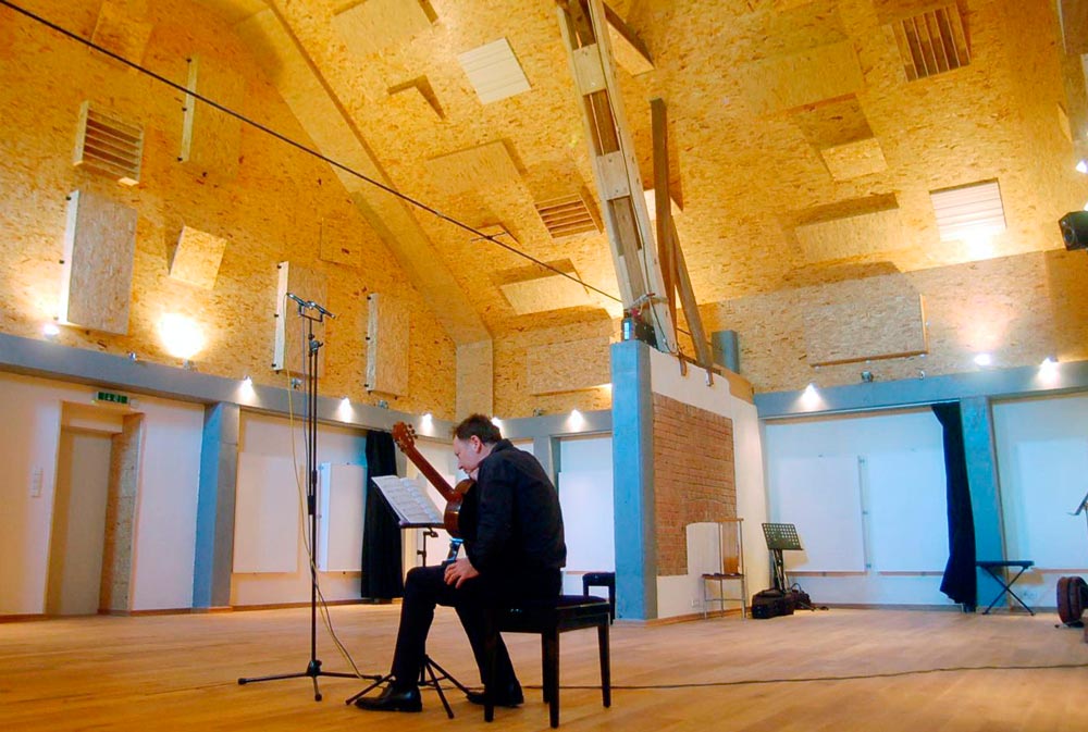 Drei Musiker sitzen im Freien, einer spielt Gitarre.